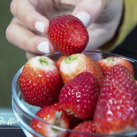 Hand greift in Glasschale mit Erdbeeren